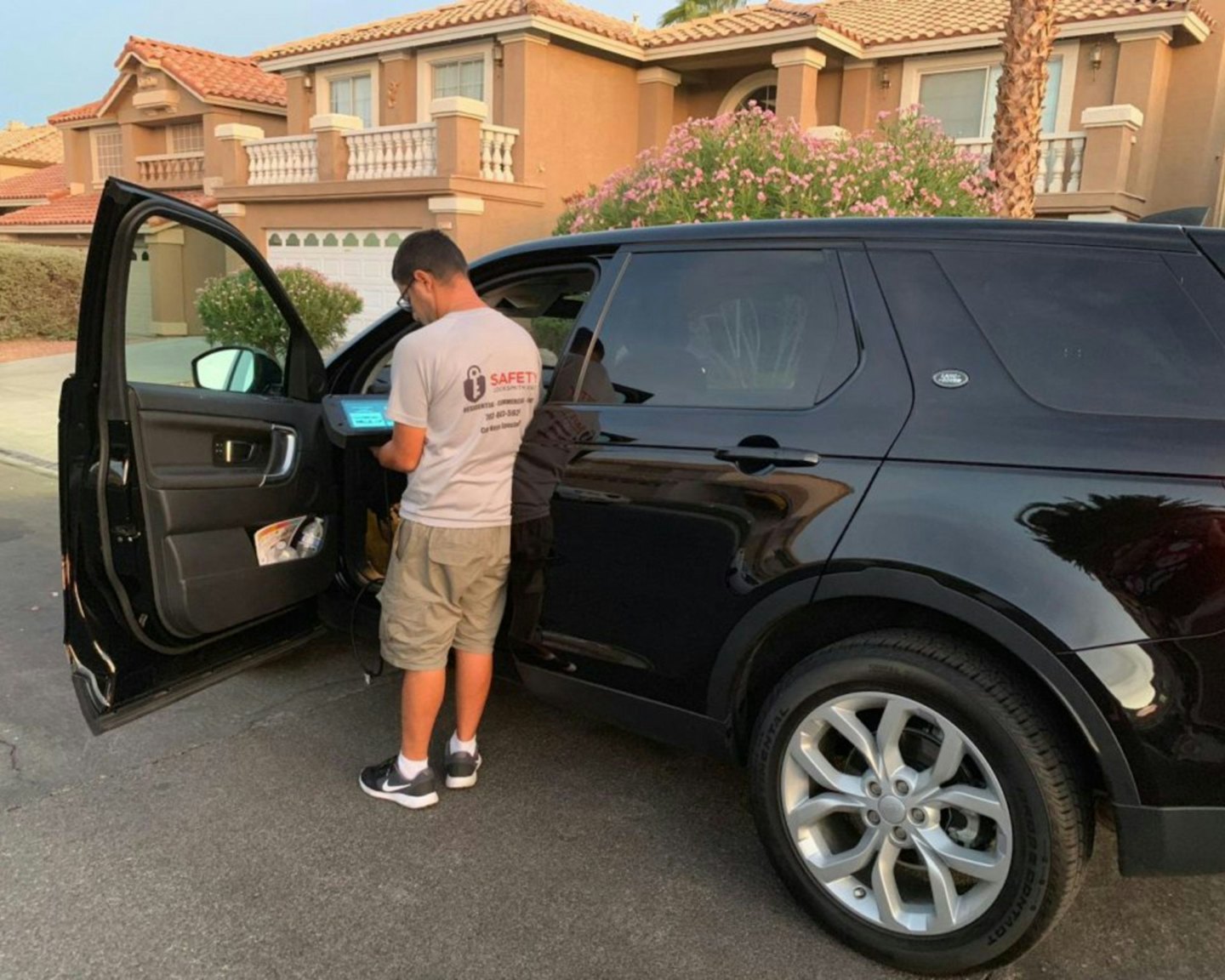 Locksmith programming car key on SUV door panel at dusk.